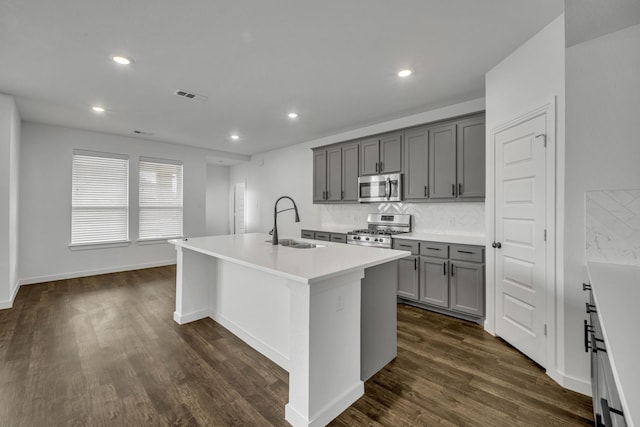 kitchen with appliances with stainless steel finishes, a center island with sink, gray cabinetry, and sink