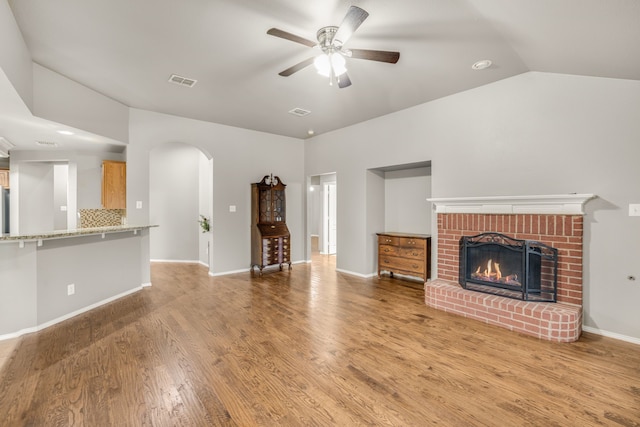 unfurnished living room featuring ceiling fan, vaulted ceiling, a brick fireplace, and light wood-type flooring