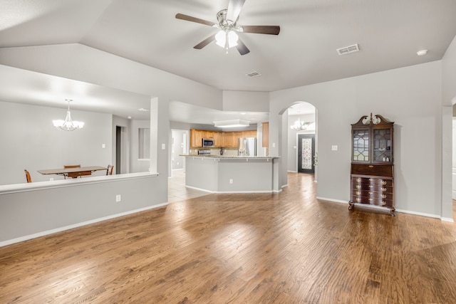 unfurnished living room featuring lofted ceiling, ceiling fan with notable chandelier, and light hardwood / wood-style flooring