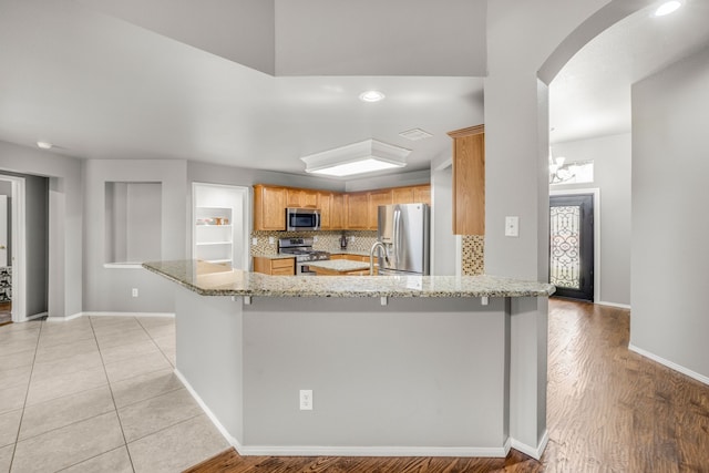 kitchen with appliances with stainless steel finishes, sink, backsplash, kitchen peninsula, and light stone countertops