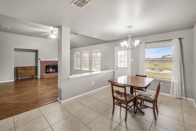 dining room featuring light tile patterned flooring, a brick fireplace, and ceiling fan with notable chandelier