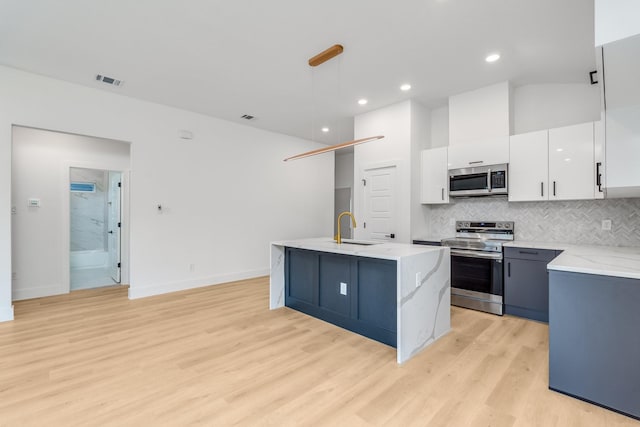 kitchen with hanging light fixtures, stainless steel appliances, a center island with sink, white cabinets, and light wood-type flooring