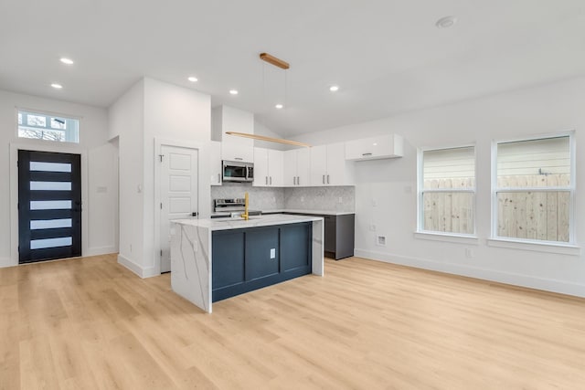 kitchen featuring a center island with sink, decorative backsplash, appliances with stainless steel finishes, decorative light fixtures, and white cabinetry