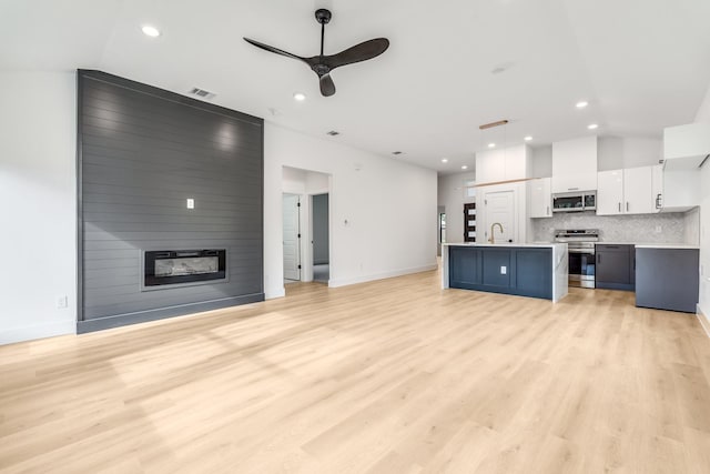 kitchen with appliances with stainless steel finishes, tasteful backsplash, decorative light fixtures, white cabinets, and an island with sink