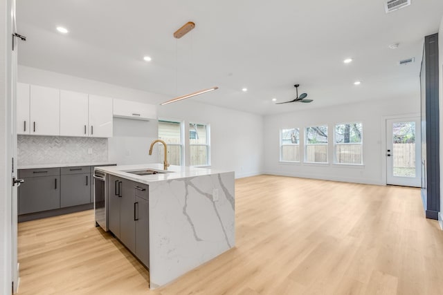 kitchen featuring backsplash, white cabinets, sink, an island with sink, and decorative light fixtures