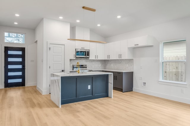 kitchen featuring pendant lighting, white cabinets, light wood-type flooring, an island with sink, and stainless steel appliances