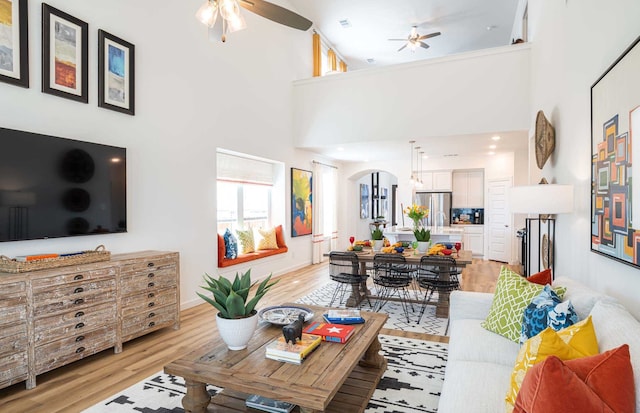 living room with a high ceiling, ceiling fan, and light hardwood / wood-style floors