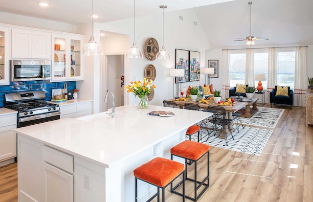 kitchen with white cabinets, vaulted ceiling, light hardwood / wood-style floors, a kitchen island with sink, and appliances with stainless steel finishes