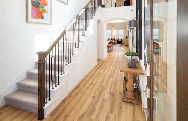 stairs with a towering ceiling, wood-type flooring, and ceiling fan