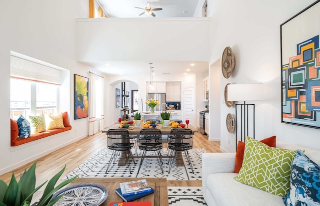 living room with a high ceiling, ceiling fan, and light hardwood / wood-style flooring