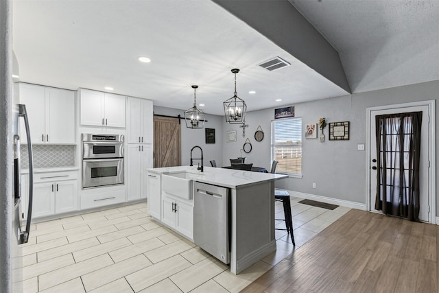 kitchen featuring white cabinetry, hanging light fixtures, stainless steel appliances, a barn door, and a kitchen island with sink