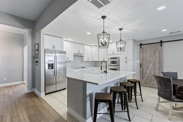 kitchen with sink, white cabinetry, stainless steel appliances, light stone countertops, and a barn door