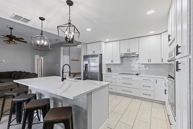 kitchen with stainless steel appliances, white cabinetry, light stone counters, and a kitchen bar