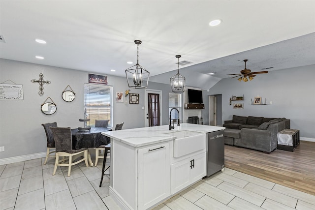 kitchen with dishwasher, white cabinetry, hanging light fixtures, light stone counters, and a center island with sink