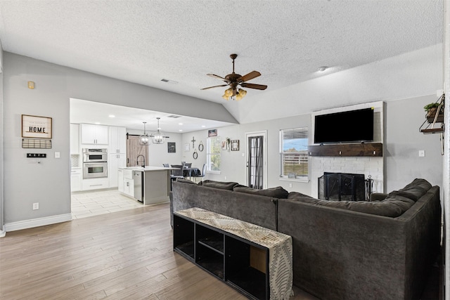 living room featuring ceiling fan with notable chandelier, sink, a textured ceiling, a fireplace, and light hardwood / wood-style floors