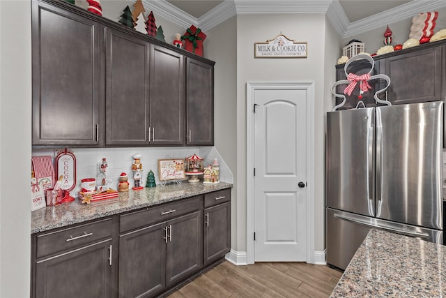 kitchen featuring stainless steel refrigerator, light stone counters, dark brown cabinets, and crown molding