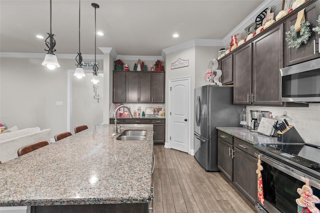 kitchen with pendant lighting, sink, a kitchen island with sink, stainless steel appliances, and light stone counters