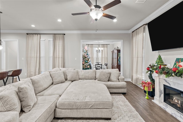 living room featuring hardwood / wood-style flooring, ceiling fan with notable chandelier, ornamental molding, and a high end fireplace