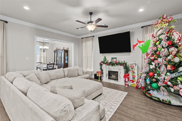 living room featuring hardwood / wood-style flooring, ornamental molding, ceiling fan with notable chandelier, and a high end fireplace