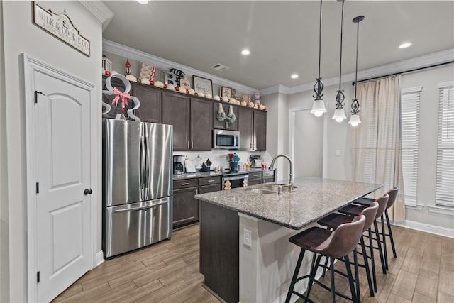 kitchen featuring sink, an island with sink, appliances with stainless steel finishes, a kitchen bar, and dark brown cabinetry