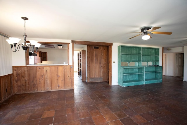 unfurnished living room featuring ceiling fan with notable chandelier and wooden walls