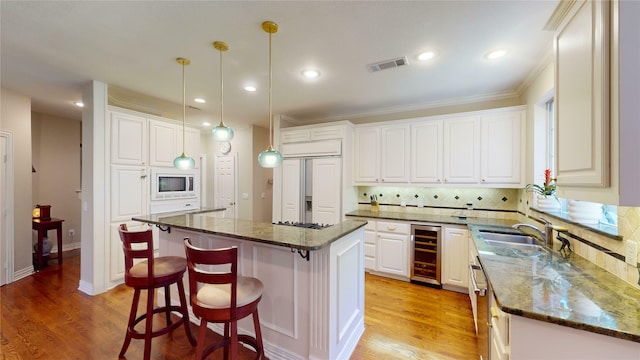 kitchen with a kitchen island, beverage cooler, sink, built in appliances, and white cabinetry