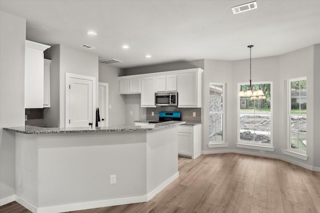 kitchen with light stone countertops, kitchen peninsula, a notable chandelier, white cabinets, and black / electric stove