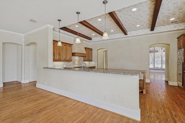 kitchen with kitchen peninsula, light stone countertops, crown molding, beam ceiling, and hanging light fixtures