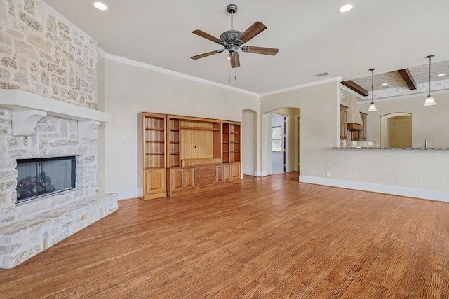 unfurnished living room featuring crown molding, hardwood / wood-style flooring, ceiling fan, a fireplace, and beamed ceiling