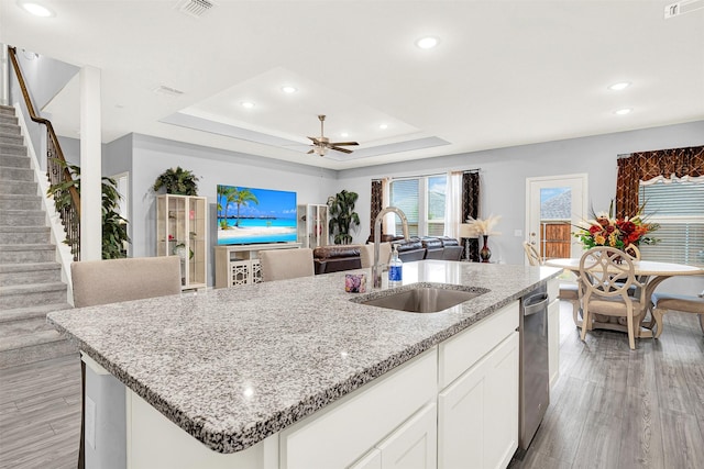 kitchen featuring sink, light stone counters, a raised ceiling, a kitchen island with sink, and white cabinets