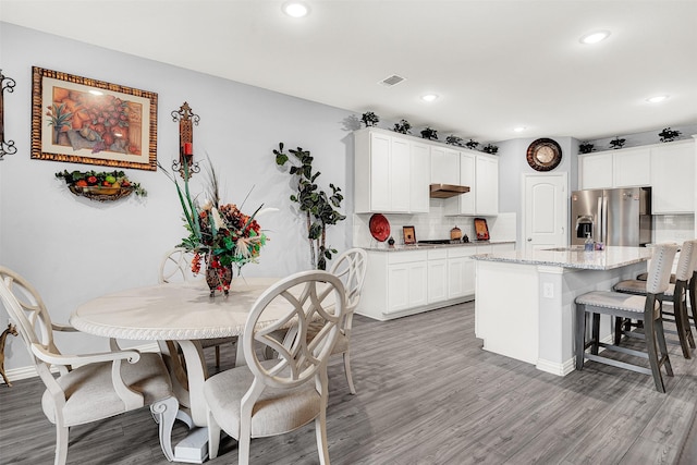 kitchen with tasteful backsplash, white cabinetry, a center island, light stone counters, and stainless steel fridge with ice dispenser