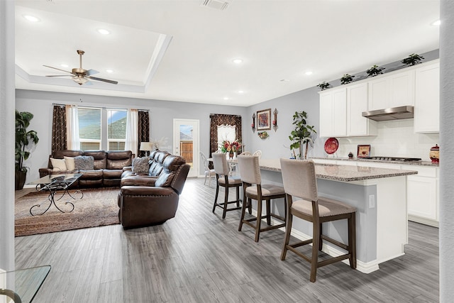 kitchen with a breakfast bar area, a kitchen island with sink, light stone counters, white cabinets, and a raised ceiling