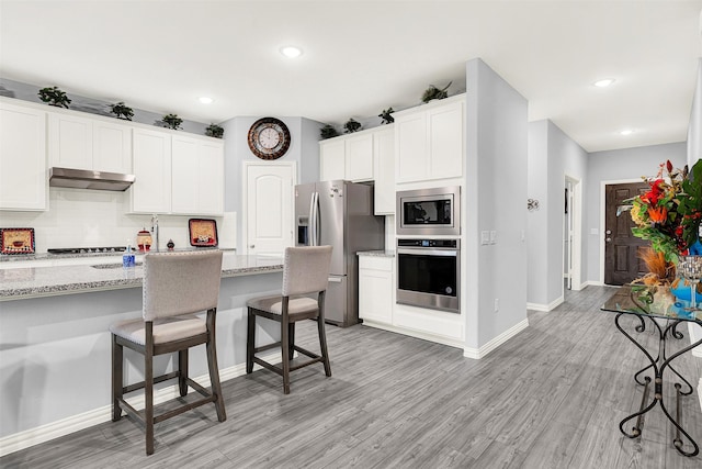 kitchen featuring white cabinetry, stainless steel appliances, light stone counters, tasteful backsplash, and light wood-type flooring