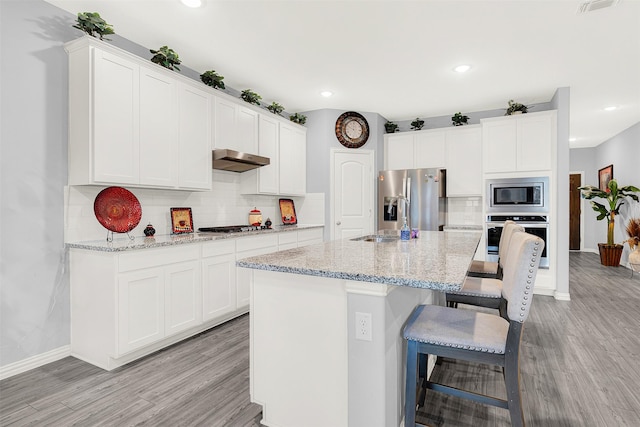 kitchen featuring white cabinetry, stainless steel appliances, light stone counters, and a center island with sink