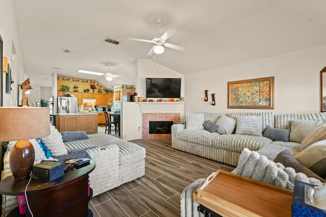 living room with a tiled fireplace, vaulted ceiling, and ceiling fan