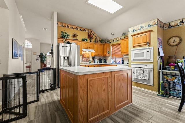 kitchen with vaulted ceiling, a kitchen island, sink, white appliances, and light hardwood / wood-style flooring