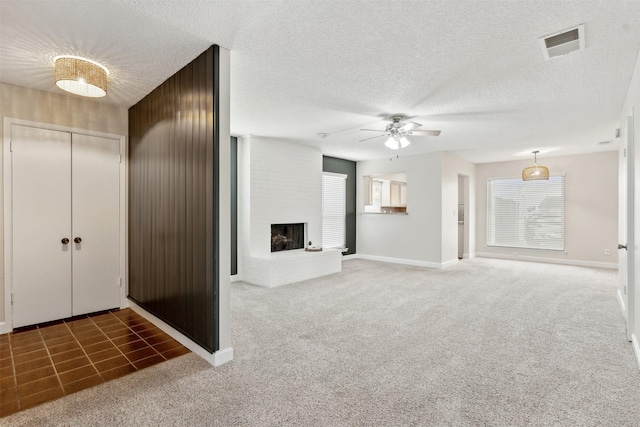 unfurnished living room featuring dark colored carpet, a textured ceiling, a brick fireplace, and ceiling fan