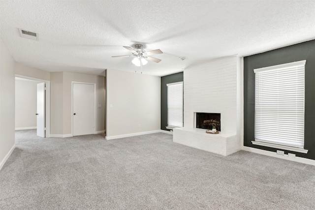 unfurnished living room with light carpet, a textured ceiling, a large fireplace, and ceiling fan