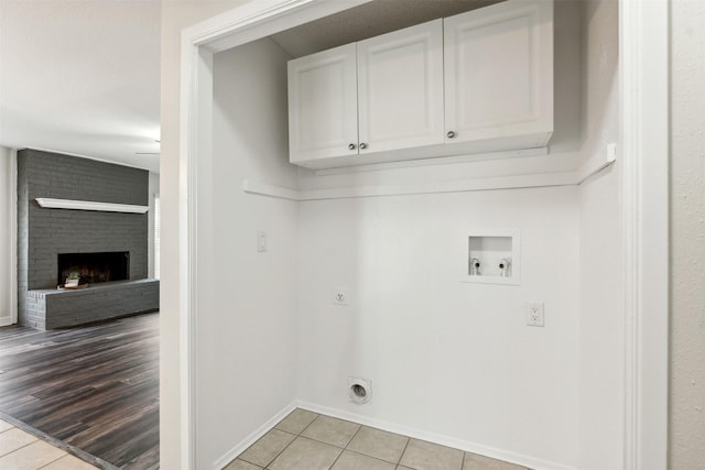 laundry area with light tile patterned floors, electric dryer hookup, hookup for a washing machine, cabinets, and a fireplace