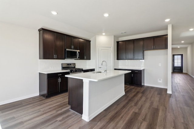 kitchen featuring a center island with sink, appliances with stainless steel finishes, sink, dark wood-type flooring, and tasteful backsplash