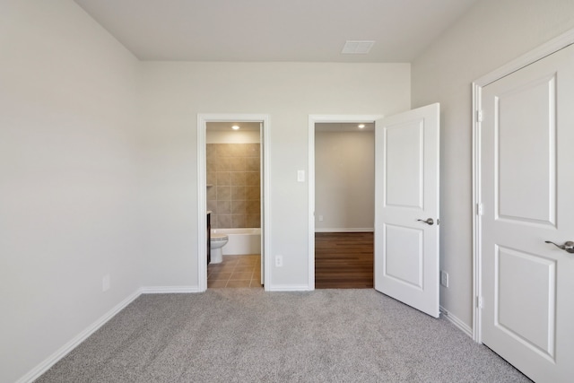 unfurnished bedroom featuring light carpet and ensuite bathroom