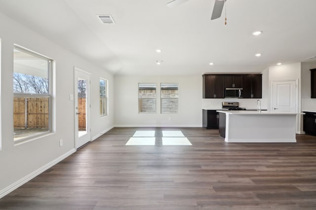 kitchen with an island with sink, stainless steel appliances, dark hardwood / wood-style flooring, dark brown cabinetry, and ceiling fan