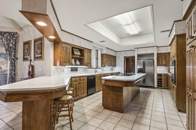 kitchen with sink, a breakfast bar, black appliances, a kitchen island, and a raised ceiling