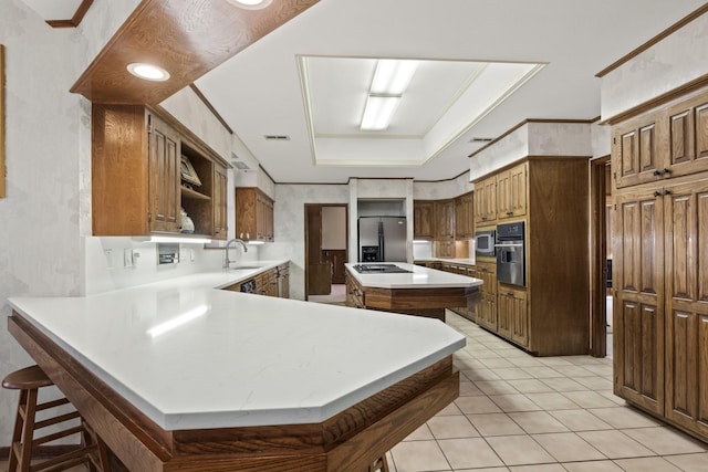 kitchen featuring a breakfast bar area, appliances with stainless steel finishes, ornamental molding, kitchen peninsula, and a raised ceiling