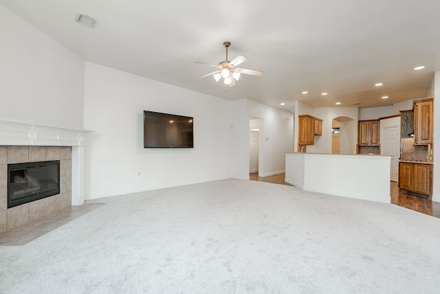 unfurnished living room with ceiling fan, light colored carpet, and a fireplace