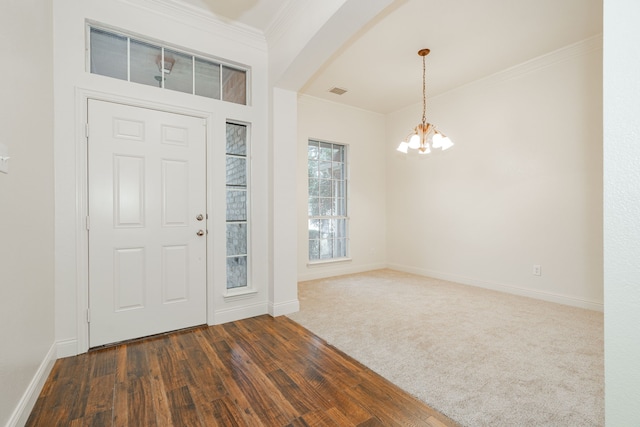 foyer with dark colored carpet, crown molding, and a notable chandelier