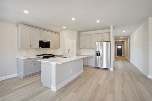 kitchen with sink, light hardwood / wood-style flooring, stainless steel appliances, and a kitchen island with sink