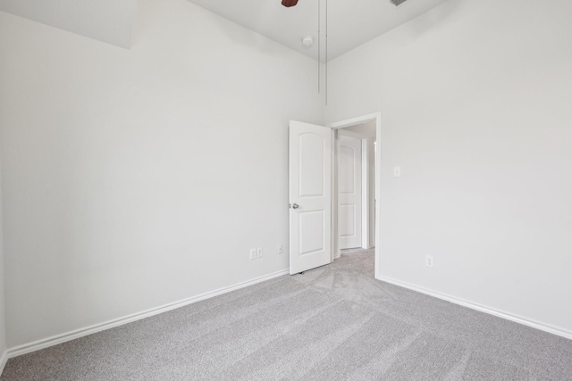 empty room featuring a high ceiling, light colored carpet, and ceiling fan