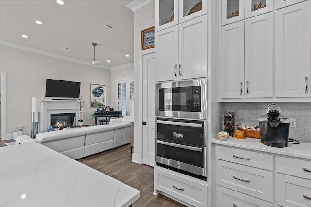 kitchen featuring decorative backsplash, ornamental molding, stainless steel oven, built in microwave, and white cabinetry