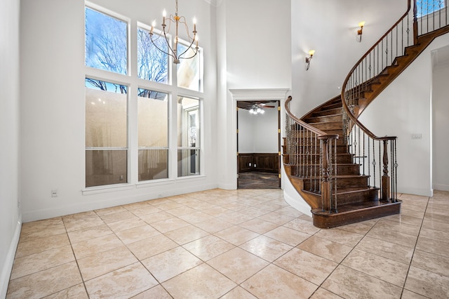 tiled entrance foyer featuring baseboards, stairs, a towering ceiling, and ceiling fan with notable chandelier